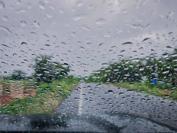 Yağmurlu bir anda arabanın ön camına yapışmış yağmur damlalarının yakın plan görüntüsü. Bulanık arka plan, su damlacıklarının güzelliğini ve yağmurlu bir günün özünü yakalayarak havayı güzelleştirir.