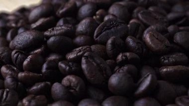 Ahşap zeminde dönen kavrulmuş kahve çekirdeklerinin koyu bir arka planda çekilmiş yakın plan videosu. Zengin doku ve derin tonlar sıcak, aromatik bir hava yaratır..