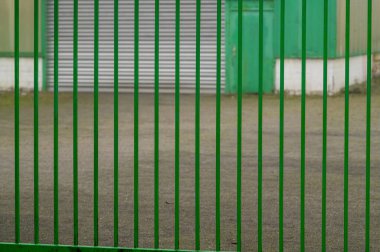 Green metal fence is protecting an industrial building with closed rolling shutter door clipart