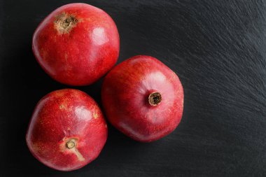 Siyah yüzeyde taze olgun narlar. Üç tane tam nar. Bol vitaminli sağlıklı bir meyve. Doğal görüntü.