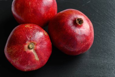 Siyah yüzeyde taze olgun narlar. Üç tane tam nar. Bol vitaminli sağlıklı bir meyve. Doğal görüntü.