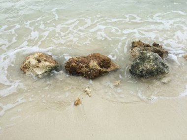 Üç küçük kaya beyaz kumsaldaki dalgaları durdurmaya çalışıyor..