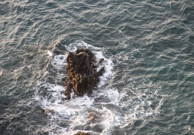 Etrafındaki deniz suyundan gelen dalgaları engellemeye çalışan bir kaya..