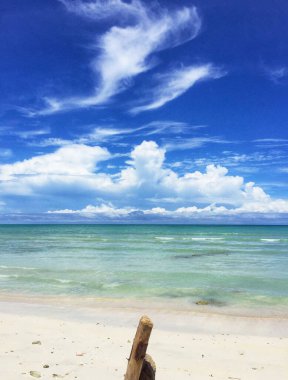 Beyaz kumsalda gün boyunca sakin manzaralar dalgaların dalgalarını ve beyaz bulutlarla süslenmiş mavi gökyüzünü görmek..