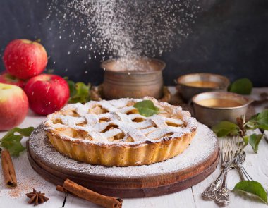 Üstünde yaprak olan bir turta, birkaç elmayla bir tabakta duruyor.