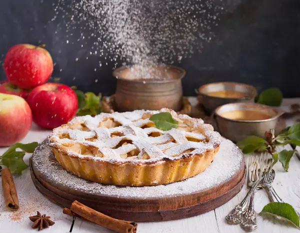 Üstünde yaprak olan bir turta, birkaç elmayla bir tabakta duruyor.