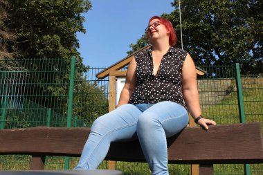 Beautiful plus size woman sitting on a bench in the park. clipart