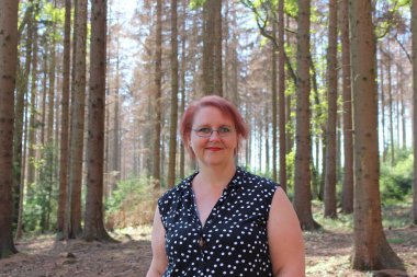 Portrait of a red-haired cheerful woman in the forest on a beautiful sunny summer day clipart