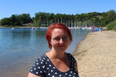 A woman with glasses and red hair stands at Lake Sorpe clipart