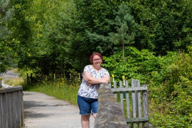 Gözlüklü ve kızıl saçlı bir kadın çitin önünde duruyor.