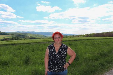 Siyah beyaz benekli tişörtlü bir kadın bir tarlada duruyor.