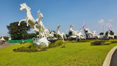 Tangerang, Endonezya - 31 Mayıs 2023: Görkemli beyaz atların heykeli açık mavi bir gökyüzüne karşı yeşil çimlerin üzerinde zıplıyor
