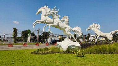 Tangerang, Endonezya - 31 Mayıs 2023: Görkemli beyaz atların heykeli açık mavi bir gökyüzüne karşı yeşil çimlerin üzerinde zıplıyor