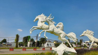 Tangerang, Endonezya - 31 Mayıs 2023: Görkemli beyaz atların heykeli açık mavi bir gökyüzüne karşı yeşil çimlerin üzerinde zıplıyor