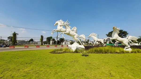 Tangerang, Endonezya - 31 Mayıs 2023: Görkemli beyaz atların heykeli açık mavi bir gökyüzüne karşı yeşil çimlerin üzerinde zıplıyor
