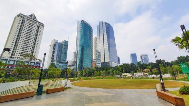 Jakarta Endonezya - 22 Ağustos 2023: Jakarta Kuningan gökdelenleri, önünde yeşil çimenlik bahçesi ve açık mavi gökyüzü olan pek çok ofis ve apartman binası