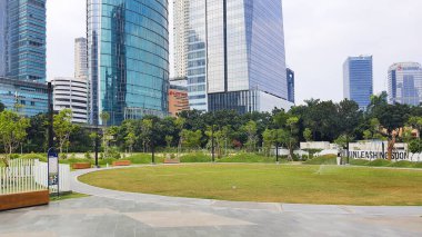 Jakarta Endonezya - 22 Ağustos 2023: Jakarta Kuningan gökdelenleri, önünde yeşil çimenlik bahçesi ve açık mavi gökyüzü olan pek çok ofis ve apartman binası