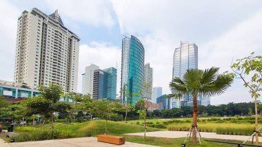 Jakarta Endonezya - 22 Ağustos 2023: Jakarta Kuningan gökdelenleri, önünde yeşil çimenlik bahçesi ve açık mavi gökyüzü olan pek çok ofis ve apartman binası