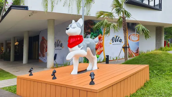 stock image Jakarta Indonesia - August 22 2023: A prancing cartoon siberian husky dog sculpture artwork on a wooden pedestal wearing a red scarf in One Satrio Strip Mall Kuningan with lush landscaping