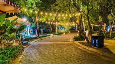 Jakarta 22 Ağustos 2023: Geceleri Şehir Ormanı Cipete 'deki restoranlar, güzel ışıklandırma, perili ışıklar, kaldırım taşı patikası, verimli peyzaj, açık hava piknik masaları. Parkta yemek yemek.