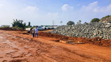 Kırmızı toprakta yol malzemesi olarak kullanılan ezilmiş taş moloz yığını. İnşaat alanındaki açık mavi arka plana karşı.