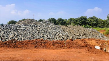 Kırmızı toprakta yol malzemesi olarak kullanılan ezilmiş taş moloz yığını. İnşaat alanındaki açık mavi arka plana karşı.