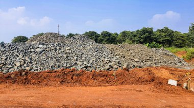 Kırmızı toprakta yol malzemesi olarak kullanılan ezilmiş taş moloz yığını. İnşaat alanındaki açık mavi arka plana karşı.