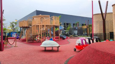 Jakarta Nov 01 2023: Parlak kırmızı kauçuk döşemeli modern oyun alanı. Gri tünel kaydırağı, kahverengi rattan ve mavi dev top. Kimse yok. çeşitli renkli teçhizatlar