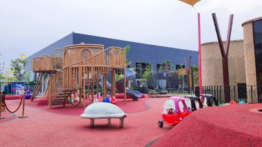 Jakarta Nov 01 2023: Parlak kırmızı kauçuk döşemeli modern oyun alanı. Gri tünel kaydırağı, kahverengi rattan ve mavi dev top. Kimse yok. çeşitli renkli teçhizatlar