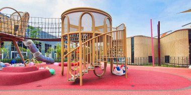 Jakarta Nov 01 2023: Parlak kırmızı kauçuk döşemeli modern oyun alanı. Gri tünel kaydırağı, kahverengi rattan ve mavi dev top. Kimse yok. çeşitli renkli teçhizatlar