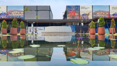 Jakarta Nov 01 2023: Beton bank ve su zambaklarıyla dolu bir havuzun önündeki saksı görüntüsü. Arkadaki binalar. simetrik yansıma Endonezya Tasarım Bölgesi PIK 2