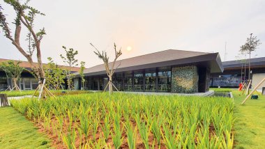 Jakarta Nov 01 2023: Cam ve desenli seramik cepheli ve önünde uzun çimenler olan bir bina. Pirinç tarlasına benziyor. Güzel peyzaj mimarisi. Günbatımı gökyüzü, insan yok. Yansıyan gölet