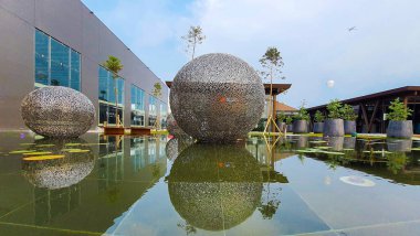 Jakarta Nov 01 2023: Yansıyan bir gölette yüzen metal top küresinin ön çekimi. Nilüferler, tropik bitkiler. Balonlar, günbatımı gökyüzü. Endonezya Tasarım Bölgesi açık hava alışveriş merkezi