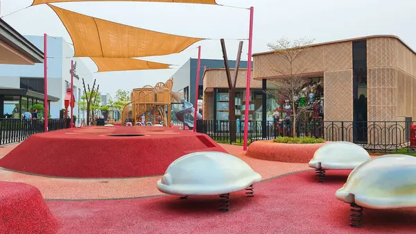 stock image Jakarta Nov 01 2023: modern playground with bright red rubber floor material. grey tunnel slide, brown rattan and blue giant ball. no people. various colorful equipments