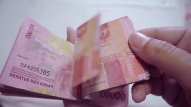 Bir adamın eli büyük miktarda IDR para birimini yelpazeliyor. Yavaş çekim parası IDR 100.000 Endonezya bankası