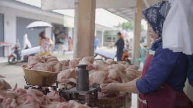 Wonosobo, Endonezya, 11 Aralık 2023 - Orta yaşlı bir kadın geleneksel bir pazarda alıcılara satmak için tavuk eti dilimliyor