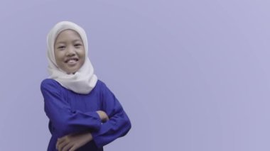 Mavi muslimah giymiş Asyalı güzel bir müslüman kızın orta boy fotoğrafı, kolları katlanmış ve gülerken kameraya bakıyordu.