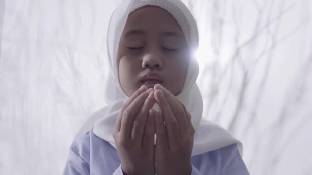 ヒジャーブを身に着けている小さなアジアの少女は 彼女の後ろにレンズフレア 白いカーテンで囲まれた祈りのジェスチャーを作ります — ストック動画