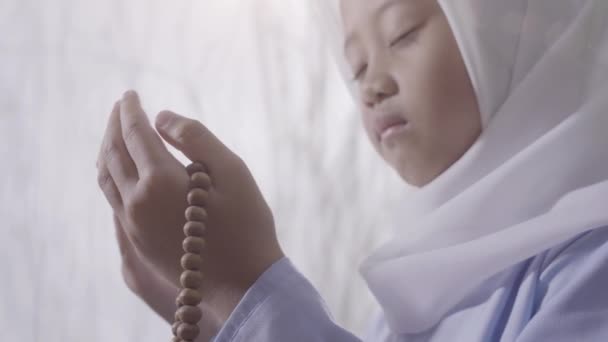 ヒジャーブを着ている小さなアジアの少女は ラマダンの聖月中に熱心に祈っている間 祈りのビーズを保持します — ストック動画