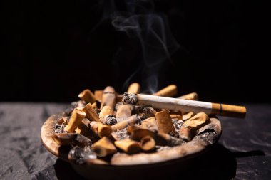 Sigara izmaritleriyle dolu kül tablasında yanan sigaralar.