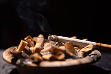 Sigaralar siyah arka planda kül tablasını yakıyor.