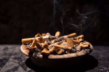 Sigara izmariti dolu kül tablasında siyah arka planda.