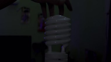 Bir erkek eli elektrik prizinde yanan bir spiral ampulü döndürür. Odadaki bir lambayı yakmak.