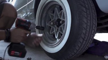 Bir adam garajdaki lastiği ingiliz anahtarıyla sökmüş.