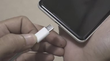 Akıllı telefona USB-C kablo makro eklentisi. El akıllı telefona beyaz USB kablosu yerleştiriyor ve sonra tekrar çıkarıyor.