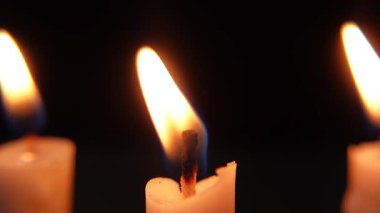 Siyah arka planda izole edilmiş yanan mumlar dizisi. Parlak mum alevleri karanlıkta parlıyor.