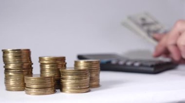 Sıraya dizilmiş altın sikkeler mali büyümeyi, yatırımı veya tasarruf yönetimini simgelerken, bir el de arkaplanda ekonomik hesaplama ve planlama için bir hesap makinesi işletiyor.