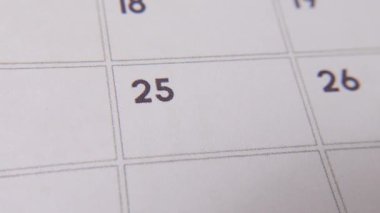 Takvimdeki 25. 'si kırmızı işaretli beyaz bir sayfada yakın plan bir makro resimle daire içine alınır. Önemli bir günü ya da hatırlatıcıyı simgeler..