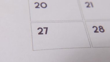 Takvimdeki 27. 'si kırmızı işaretli beyaz bir sayfada yakın plan bir makro resimle çevrelenmiş. Önemli bir günü ya da hatırlatıcıyı simgeliyor..