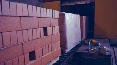 Plastiğe paketlenmiş paletlerdeki kırmızı tuğlalar. Paketlenmiş tuğlaların fabrikadan nakledildiği nakliye hattı. 4k.